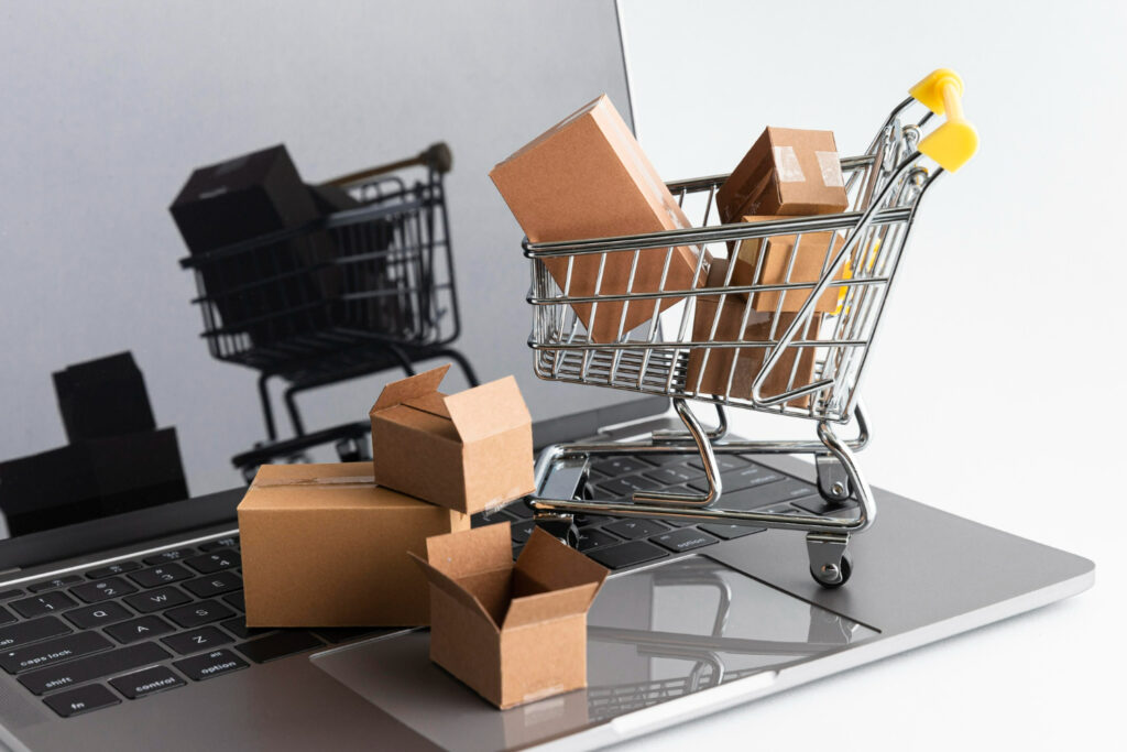 Imagem ilustrativa sobre como fazer dropshipping em segurança mostrando um pequeno carrrinho de compras e algumas caixas de papelão sobre um notebook, representando as compras online feitas nesse modelo de negócios.