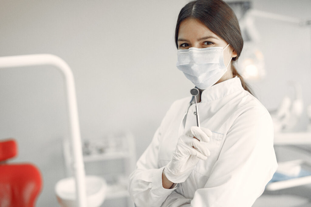 Imagem ilustrativa sobre contabilidade para dentistas mostrando uma dentista jovem, usando trajes cirúrgicos, mas sorrindo por baixo da máscara.